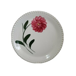 May include: White ceramic dinner plate with a pink flower and green leaves painted on the side.