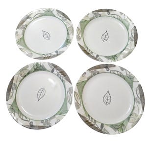 May include: Four white ceramic plates with a leaf design in the center. The plates have a decorative border with green, gray, and white leaf and floral patterns. The plates are suitable for serving food.