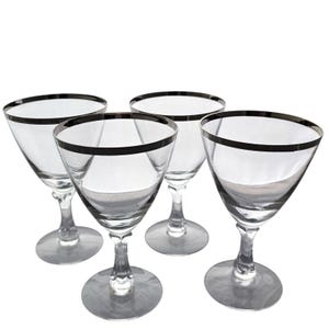Peut inclure: Quatre verres à pied transparents avec un bord argenté. Les verres ont un design classique avec un large bol et un pied fin. Les verres sont disposés en groupe, parfaits pour servir des boissons lors d'une réception.