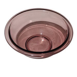 May include: A clear, round, glass mixing bowl in a soft, dusty rose color. The bowl has a wide rim and a slightly textured interior base with concentric circles. The bowl is designed for mixing and food preparation.