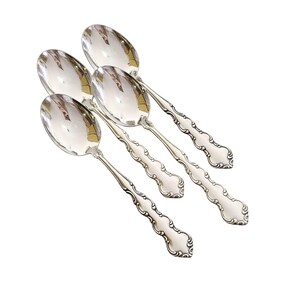 May include: Four silver spoons with ornate, curved handles and oval bowls. The spoons are arranged diagonally, showcasing their reflective surfaces. The handles feature a detailed, scrolling design, adding a touch of elegance to the silverware.