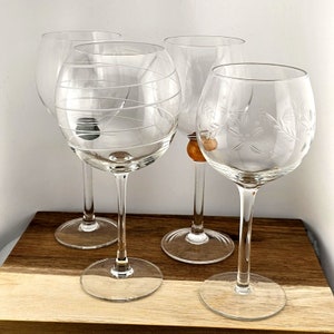 May include: Four clear glass wine glasses with different etched designs. The glasses are on a wooden surface.