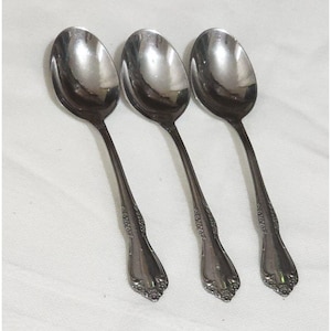 May include: Three silver spoons with ornate handles. The spoons have a rounded bowl and a long, slender handle with a decorative design.