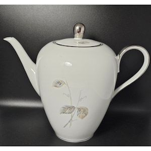 May include: White porcelain teapot with a silver lid and a floral design in gold and gray.