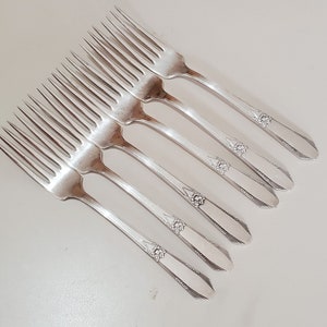 May include: Set of six silver forks with ornate handles. The forks have a traditional design with a rounded handle and a decorative pattern.