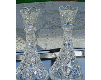 May include: A pair of clear glass candle holders featuring a flared base and a scalloped top rim. The body of each holder is decorated with a geometric cross-hatch pattern that catches the light, creating a faceted appearance throughout the glass.