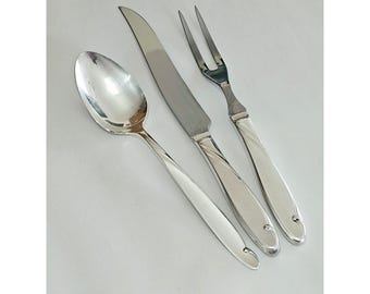 May include: A set of three stainless steel utensils including a dinner spoon, a dinner knife, and a two-pronged carving fork. Each piece features a polished silver finish and a smooth, tapered handle with a small, rounded decorative detail at the end.