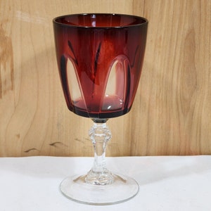 May include: A deep red wine glass with a clear stem and base. The glass has a faceted design and a rounded bowl.