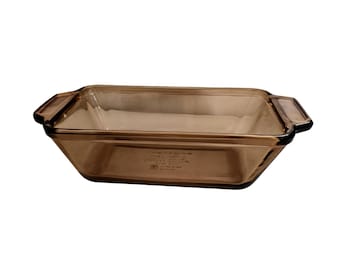May include: A rectangular baking dish made of translucent brown glass. The dish features integrated handles on both short ends and has a smooth, polished finish. Embossed text is visible on the interior base of the glass bakeware.