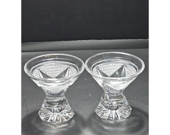 May include: A pair of clear glass dessert bowls featuring a wide, flared rim and a thick, pedestal base. The exterior of the bowls displays a detailed diamond-cut pattern, while the base is decorated with a radiating starburst design.