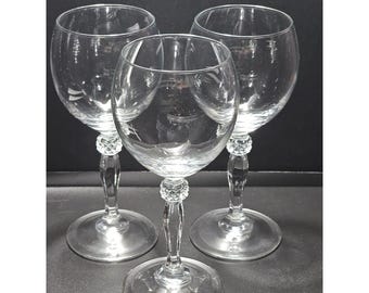 May include: Three clear glass wine glasses with rounded bowls and stems featuring a textured, diamond-cut pattern detail near the top of the stem. Each glass has a smooth, circular base and a transparent, colorless finish throughout the design.