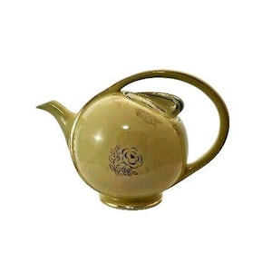 May include: A vintage, light green teapot with a rounded body and a curved handle. The teapot features a black floral design and gold trim. The spout and lid are also light green. A classic piece for tea lovers.