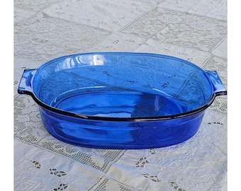 May include: An oval-shaped cobalt blue glass baking dish featuring integrated handles on both sides. The dish is constructed from transparent, deep blue glass with a smooth, polished finish and a wide, open rim design for serving or baking.