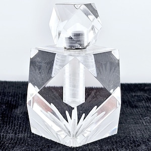 May include: A clear glass perfume bottle with a faceted stopper and a geometric design. The bottle has a starburst pattern etched into the bottom.