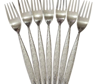 May include: A set of seven silver-toned metal forks arranged in a fan shape. Each fork features four tines and a handle decorated with a repeating embossed geometric pattern consisting of small, interconnected four-petaled floral shapes.