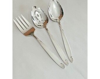 May include: A set of three silver-toned serving utensils consisting of a four-tined fork, a slotted spoon with a decorative cutout pattern, and a solid oval-shaped spoon. Each piece features a smooth, polished finish and a curved handle end.