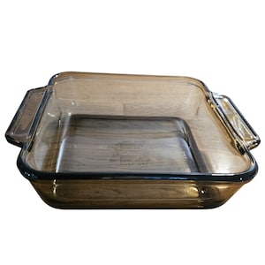 May include: A rectangular, amber-colored glass baking dish with two handles. The dish has a slightly rounded rim and is designed for oven use. The glass is transparent, allowing visibility of the contents. The dish is approximately 13 inches long and 9 inches wide.
