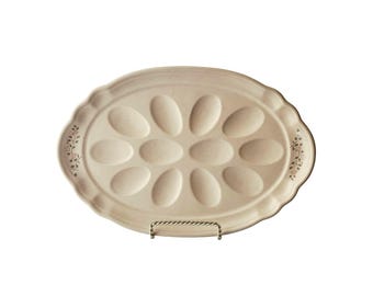 May include: An oval-shaped, off-white ceramic egg platter featuring twelve recessed egg-shaped indentations. The rim has a scalloped edge and is decorated with small, delicate floral sprigs in muted pink and green tones on both sides.
