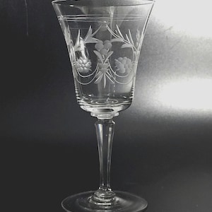 May include: A clear, stemmed wine glass with etched floral and leaf designs. The glass features a slender stem and a wide bowl, with delicate patterns around the bowl's rim and body. The glass is made of clear glass.