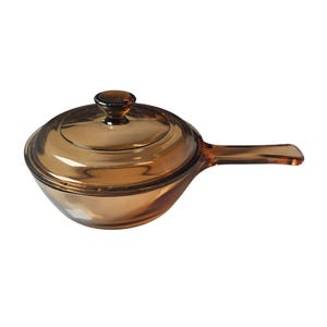 May include: Amber-colored glass saucepan with a lid and a handle. The cookware has a rounded shape and a matching lid with a small knob. The handle extends from the side, offering a secure grip. This kitchenware is ideal for cooking.