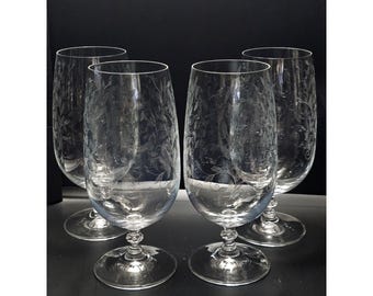 May include: A set of four clear glass goblets featuring delicate etched floral and vine patterns on the bowls. Each glass has a smooth, rounded rim, a tapered body, and a stem with a distinct twisted glass detail resting on a circular base.