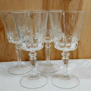 May include: Set of four clear glass wine glasses with a cut glass design. The glasses have a tall, slender stem and a wide bowl.