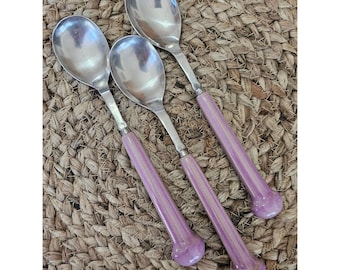 May include: Three silver-toned metal spoons with long, cylindrical handles in a glossy, light purple finish. Each spoon features a smooth, rounded bowl and a flared, rounded end on the handle, creating a uniform set of cutlery for dining.