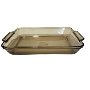 May include: A brown glass baking dish with rounded corners and handles. The dish is made of tempered glass and is safe for use in the oven, microwave, and freezer.