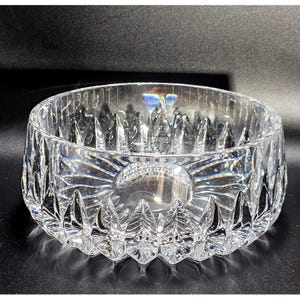 May include: A clear, round glass bowl featuring a faceted exterior with a repeating leaf-like pattern around the base and vertical fluting along the upper rim. The heavy crystal construction creates distinct light refractions and reflections.