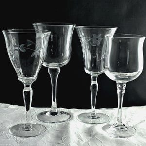 May include: Four clear glass wine glasses with etched floral patterns. The glasses have different bowl shapes and stem designs, with a round base. The background is black and white, emphasising the transparency of the glassware.