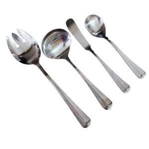 May include: A set of four stainless steel serving utensils. The set includes a salad fork, a ladle, a butter knife, and a spoon. Each utensil has a long, slender handle and a polished, reflective surface.