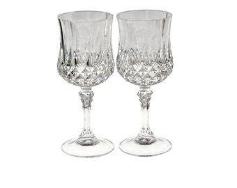 May include: A pair of clear glass goblets featuring a faceted diamond-cut pattern on the lower bowl and a textured, multi-faceted stem. Each glass has a smooth, flared rim and a circular base, reflecting light through the intricate geometric design.