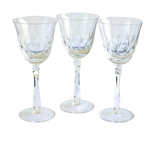 May include: Three clear crystal wine glasses with etched floral designs. Each glass has a rounded bowl, a slender stem, and a circular base. The glasses are arranged in a row against a white background.