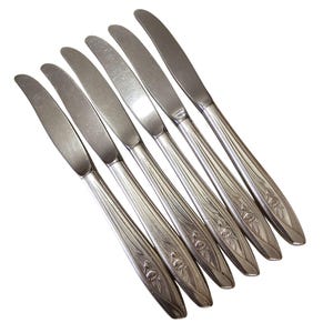 May include: Set of six silver-plated dinner knives with floral designs. The knives have a slightly curved blade and a rounded handle.