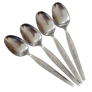 May include: Four stainless steel spoons with oval bowls and long, slender handles. The handles are decorated with a floral pattern. The spoons are arranged diagonally against a white background.