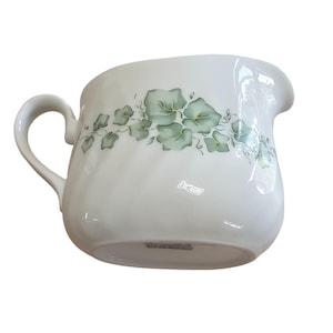 May include: White ceramic creamer with a curved handle and a spout. The creamer is decorated with a green and gray ivy leaf pattern. The creamer is designed for serving cream or milk.