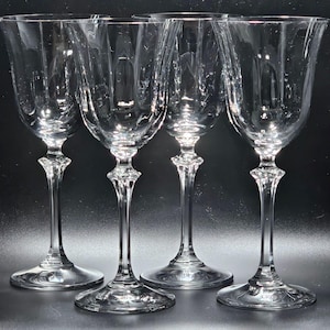 May include: Four clear glass wine glasses with a delicate stem and a wide bowl. The glasses are arranged in a row on a black surface.