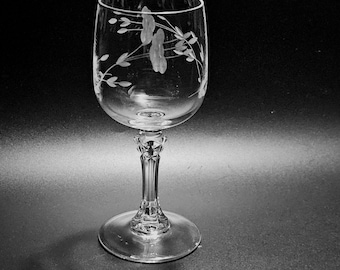 May include: A clear glass wine goblet featuring a delicate etched floral pattern on the bowl. The stem has a faceted, multi-sided design that connects to a smooth, circular base. The glass is transparent with a polished finish throughout.