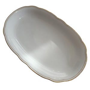 May include: An oval-shaped, white serving dish with a scalloped edge and a thin gold trim. The dish has a smooth, glossy surface and is empty. The design is simple and elegant, suitable for serving appetizers or desserts.