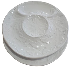 May include: White ceramic serving dish with a floral and leaf design. The dish has a central bowl and two side compartments. The design is embossed on the surface. The dish is stacked on top of a similar, but simpler, white plate.
