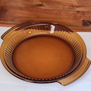 May include: A brown glass pie plate with two handles. The plate has a fluted edge and a smooth interior.