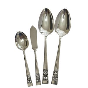 May include: A set of four silver-toned metal utensils including two large spoons, one smaller spoon, and one flat-bladed spreader. Each piece features a smooth, polished bowl or blade and a handle decorated with a detailed floral relief pattern.