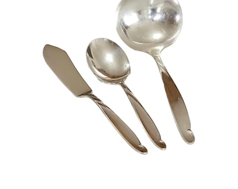 May include: A set of three polished silver-toned metal utensils consisting of a flat-bladed spreader knife, a small oval-bowled spoon, and a large round-bowled ladle, each featuring a smooth, tapered handle with a curved, hook-like end.