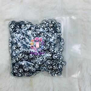 May include: A clear plastic bag filled with black and white round resin charms featuring a smiling Jack Skellington face from the Nightmare Before Christmas movie.