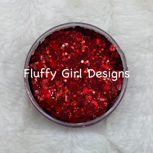 May include: A close-up of a clear jar filled with red glitter. The glitter is a mix of fine and chunky pieces. The jar is labeled "Fluffy Girl Designs".