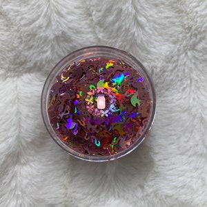 May include: A clear jar filled with iridescent pink glitter featuring various shapes, including flamingos, butterflies, and flowers.