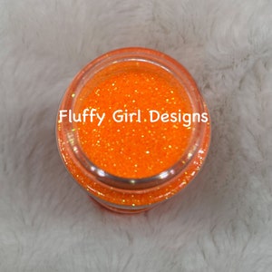 May include: A small glass jar filled with bright orange glitter. The jar has a clear lid and the text "Fluffy Girl Designs" is printed on the label.