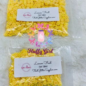 May include: Two clear plastic bags filled with yellow lemon slice shaped confetti. The bags have labels that read "Lemon Fruit (Not Edible) ThatGlitterSupplier.com" and "Fluffy Girl Designs".