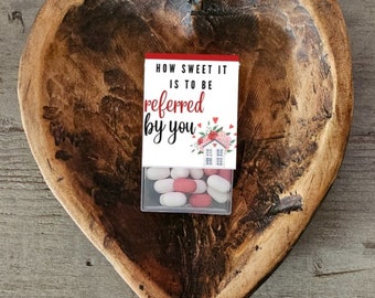 May include: A small box of candy with a red and white label that says "How sweet it is to be referred by you". The box is sitting in a wooden heart-shaped bowl.