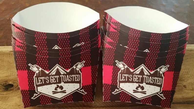 May include: A stack of red and black plaid paper cups with a white interior. The cups have a brown logo that says "Let's Get Toasted" with a campfire and a mountain design.